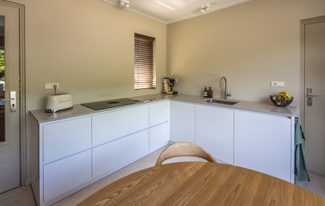 witte L vormige keuken met greeploos design