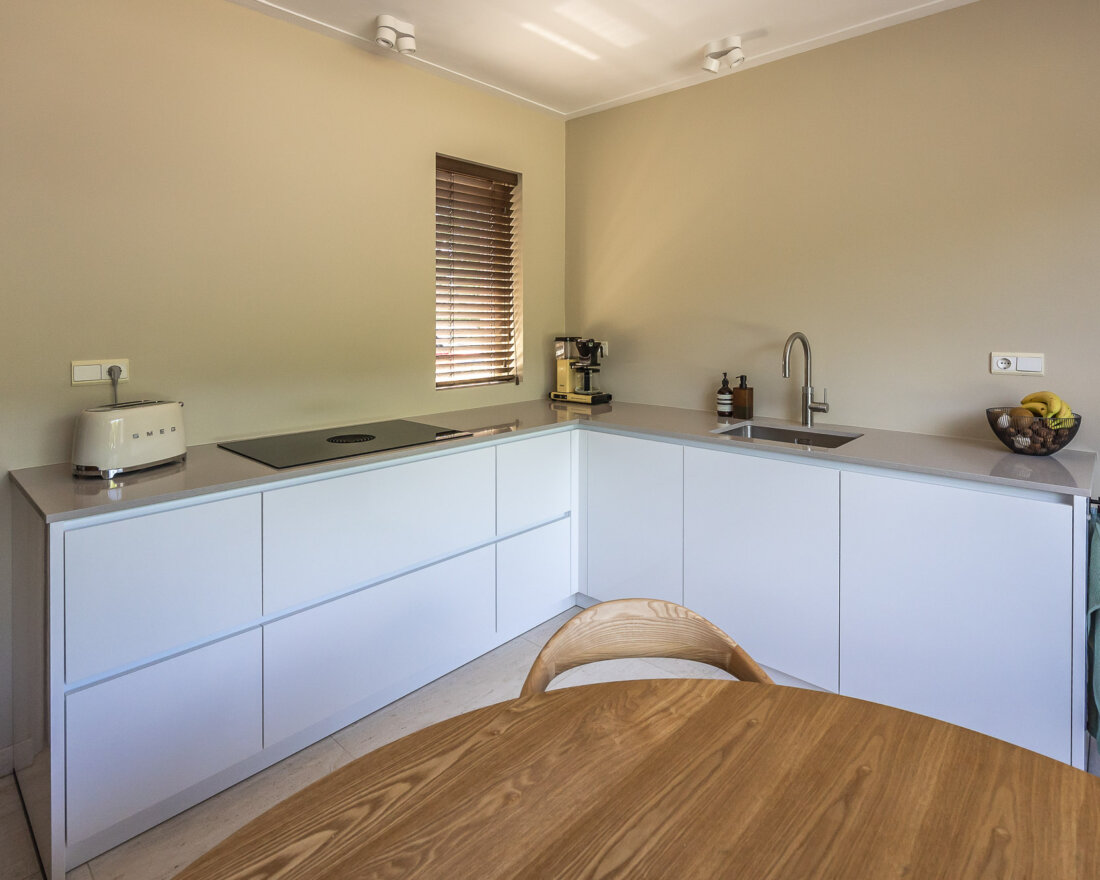 witte L vormige keuken met greeploos design